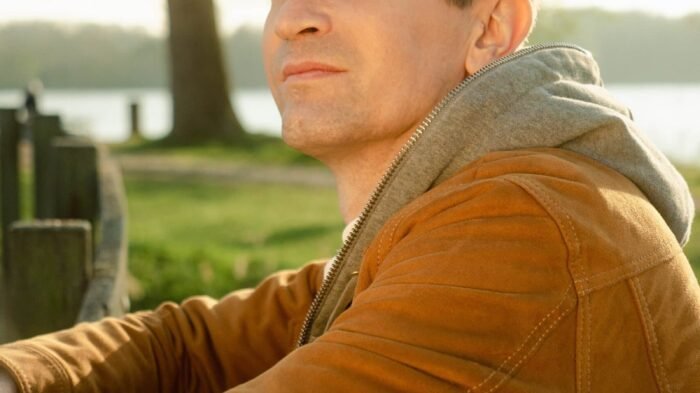 Baptiste Valloy en veste marron claire cappuyé sur ujne barrière