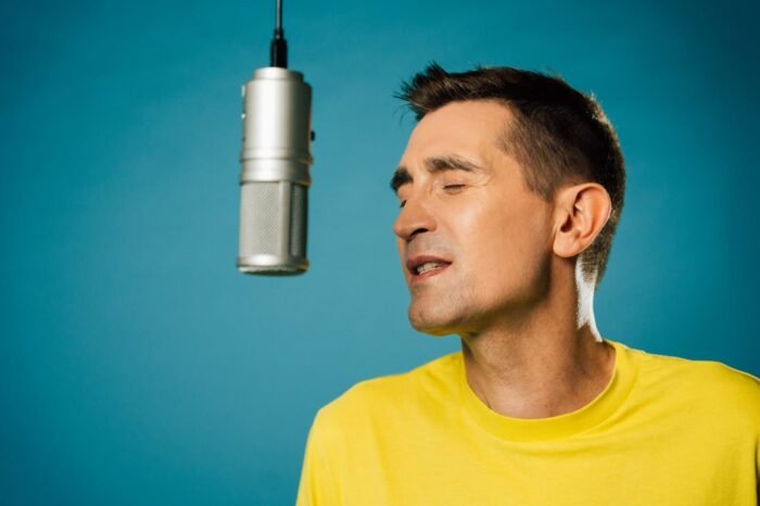 Baptiste Valloy en tee-shirt jaune, les yeux fermés face à un micro suspendu