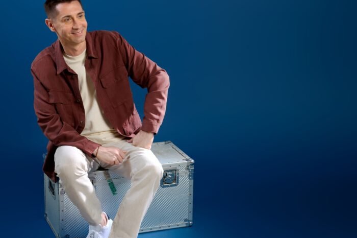 Baptiste Valloy assis sur une caisse en métal sur fond bleu comme la pochette de l'album